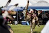 A participant carries a feather-adorned staff across the dance arena at the San Manuel Pow Wow at CSUSB Floral beadwork and long fringe decorate the participants regalia